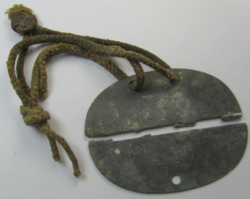 Zinc-based - albeit broken in two parts - WH (Heeres) 'Artillerie'-related ID-disc bearing the clearly stamped unit-designation that reads: 'Schw.Art.Abt.(mot.) 53 - 6 Bttr.' and that comes mounted onto its period cord as issued- and/or worn