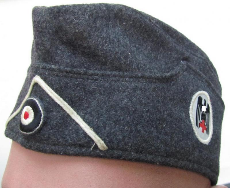 Attractive, typical darker-greyish-blue-coloured, so-called: German Red Cross (ie. 'Deutsches Rotes Kreuz' or: 'DRK' EM- (ie. NCO-) type side-cap (ie. 'Schiffchenmütze für Mannschaften u. Unteroffiziere des deutschen Rotes Kreuzes')