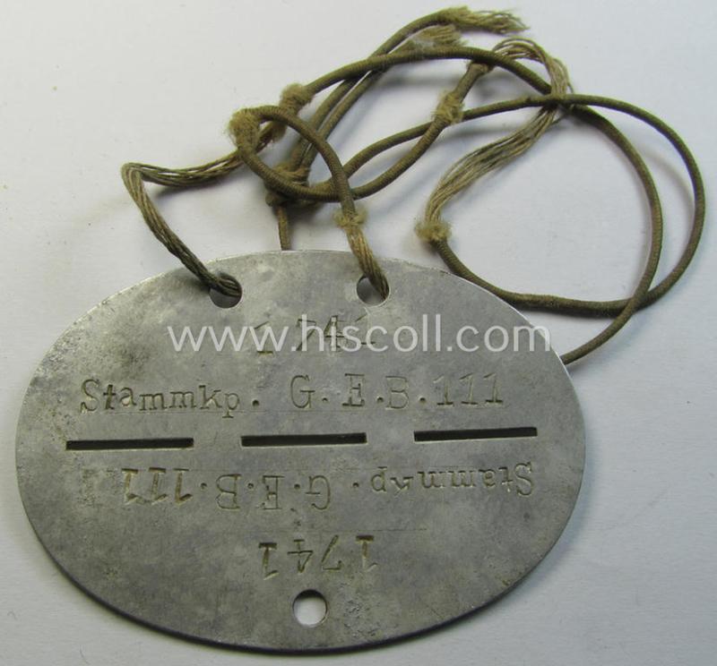 Attractive, aluminium-based WH (Heeres) (ie. 'Grenadiere'-related) ID-disc bearing the clearly stamped unit-designation that reads: 'Stammkp. G.E.B.111' and that comes still mounted onto its (period-attached) cord as issued- and/or worn