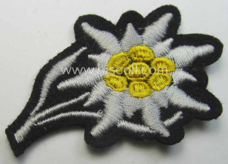 Waffen-SS-pattern, black-coloured M43-cap-insignia (ie. 'Mützenabzeichen') depicting an: 'Edelweiss'-flower as used by the various 'Gebirgsjäger'- (ie. mountain-troops-) related divisional-staff