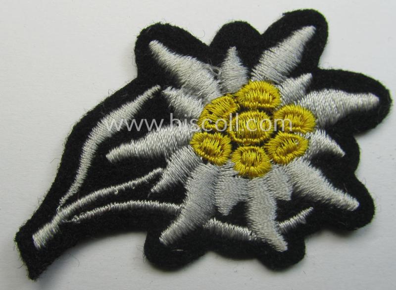 Waffen-SS-pattern, black-coloured M43-cap-insignia (ie. 'Mützenabzeichen') depicting an: 'Edelweiss'-flower as used by the various 'Gebirgsjäger'- (ie. mountain-troops-) related divisional-staff