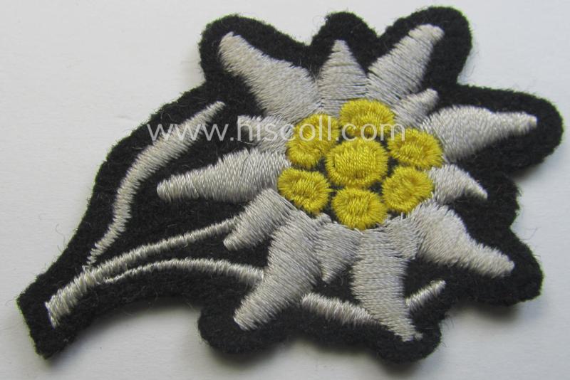 Waffen-SS-pattern, black-coloured M43-cap-insignia (ie. 'Mützenabzeichen') depicting an: 'Edelweiss'-flower as used by the various 'Gebirgsjäger'- (ie. mountain-troops-) related divisional-staff