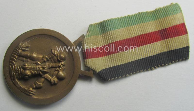 Golden-bronze-coloured- (and I deem 'Buntmetall'-based-) example of a: 'Deutsch-Italienische Feldzugsmedaille' (or: German-Italian campaign-medal) that comes mounted onto its (regular-sized) piece of original (and minimally faded!) ribbon