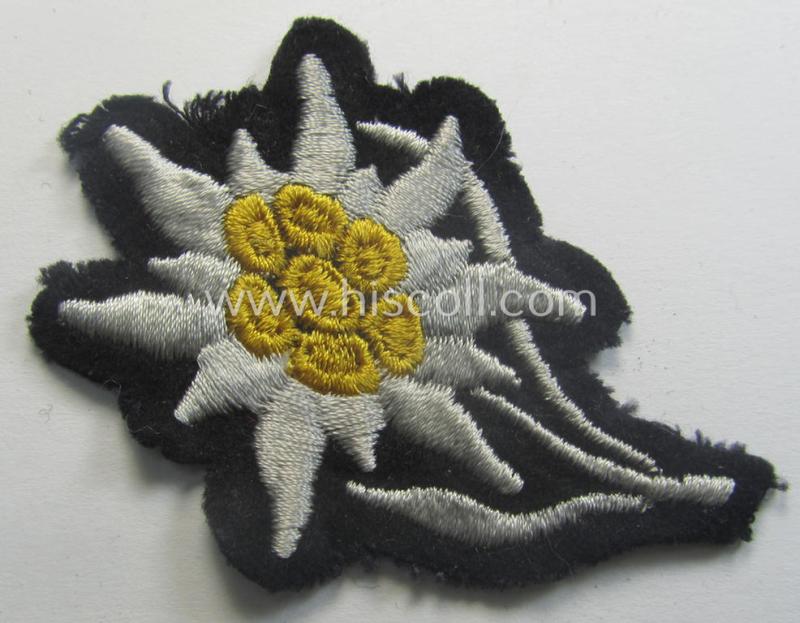 Waffen-SS-pattern, black-coloured M43-cap-insignia (ie. 'Mützenabzeichen') depicting an: 'Edelweiss'-flower as used by the various 'Gebirgsjäger'- (ie. mountain-troops-) related divisional-staff