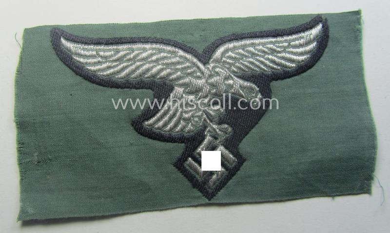 WH (Luftwaffe) officers'- (ie. evt. NCO-) type breasteagle (ie. 'Brustadler') as was executed in neatly machine-woven silver-coloured thread (ie. 'flatwire-style') onto a darker-blue- (ie. field-grey-) coloured- and/or linnen-based background