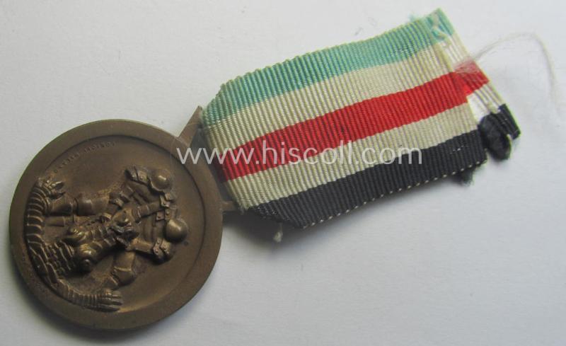 Golden-bronze-coloured- (and I deem 'Buntmetall'-based-) example of a: 'Deutsch-Italienische Feldzugsmedaille' (or: German-Italian campaign-medal) that comes mounted onto its (regular-sized) piece of original (and hardly faded!) ribbon
